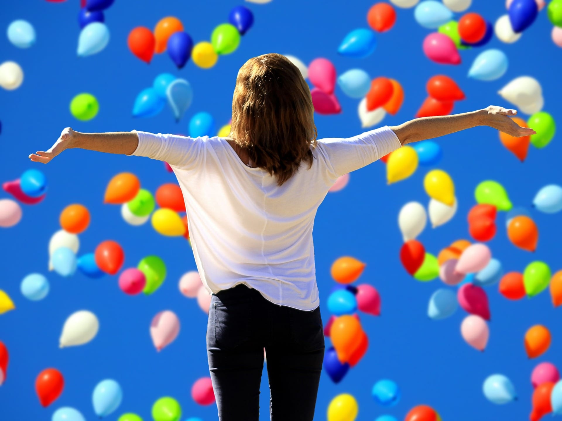 A woman triumphantly facing balloons as they fly through the sky.