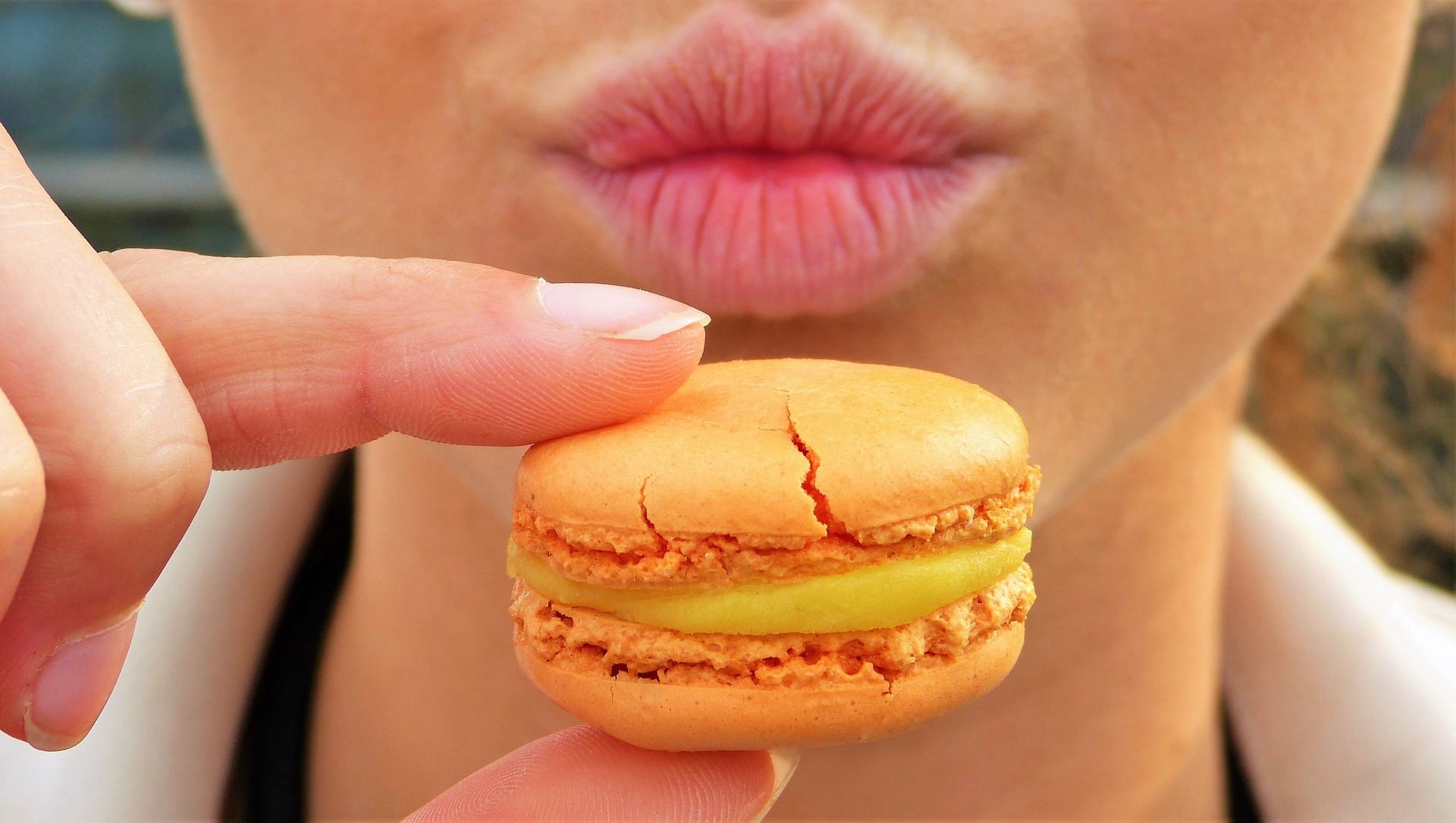 A person holding a macaron and making a cheeky face.