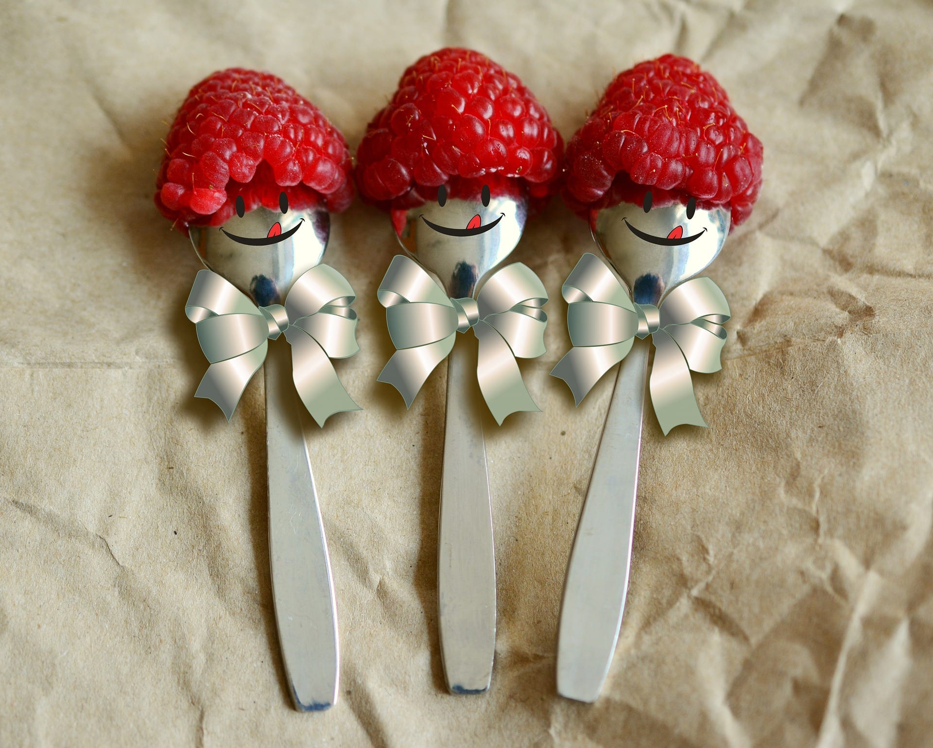 Spoons with happy faces and bows wearing raspberries for hats.