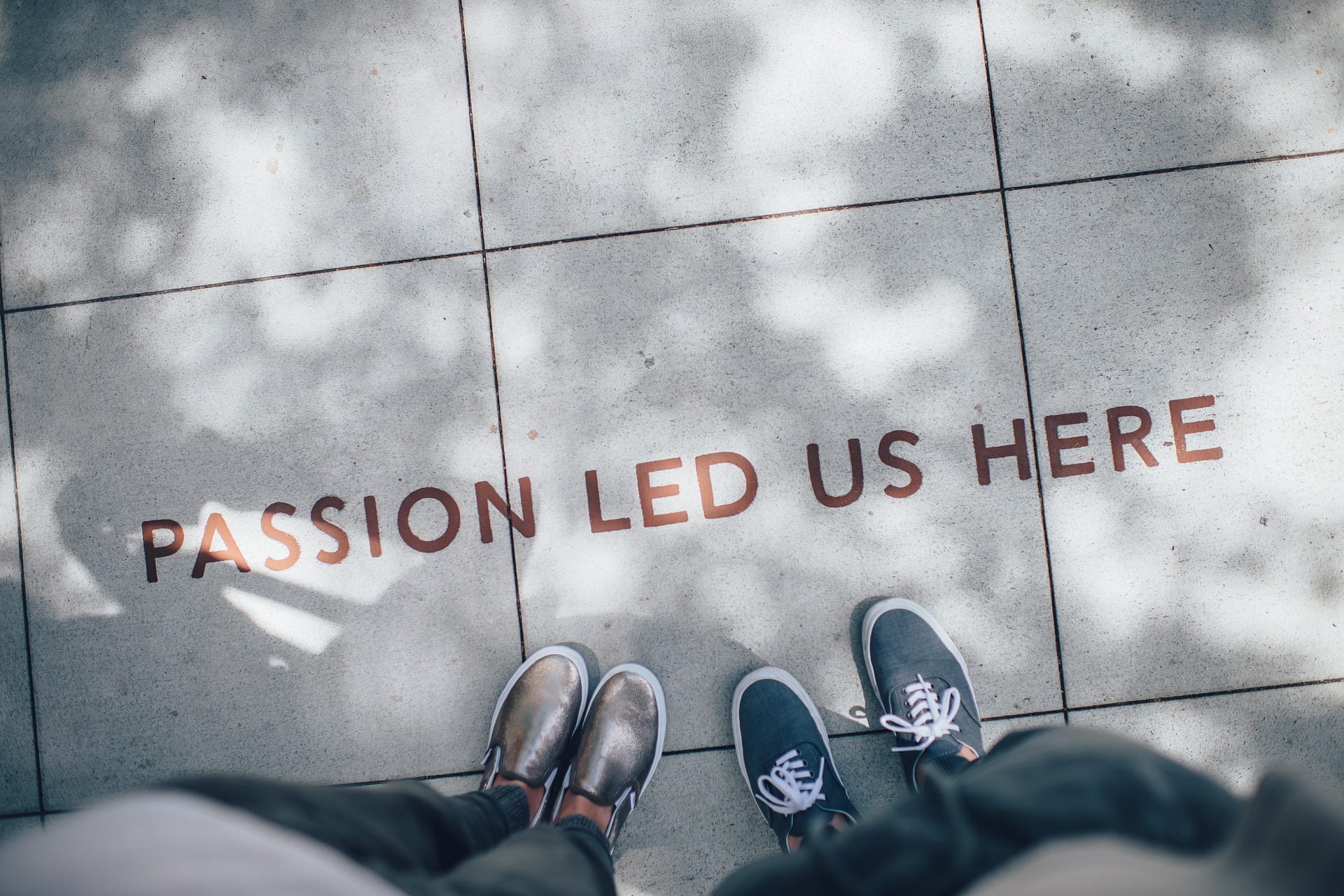 Some feet pointing to the words "PASSION LED US HERE" written on the ground.