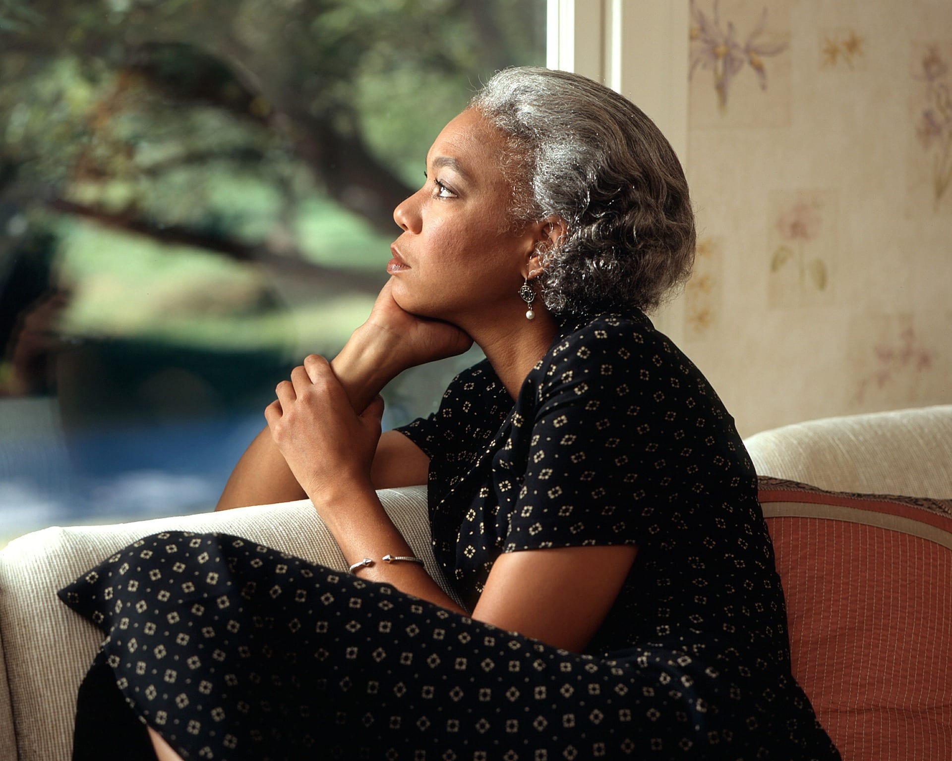 A pensive older black woman looking out a window.