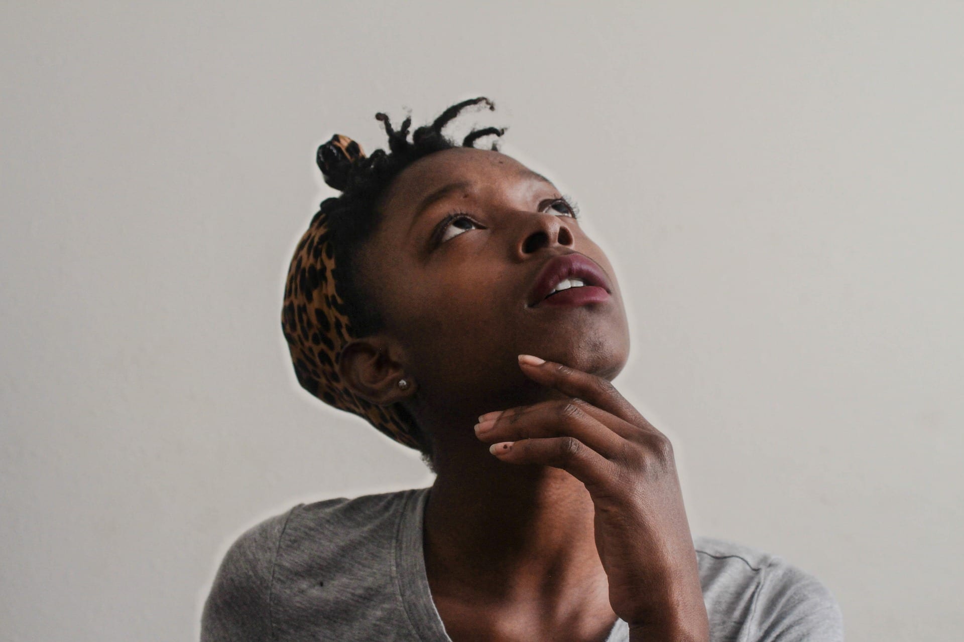 A young dark-skinned woman looking up in a pensive sort of way.